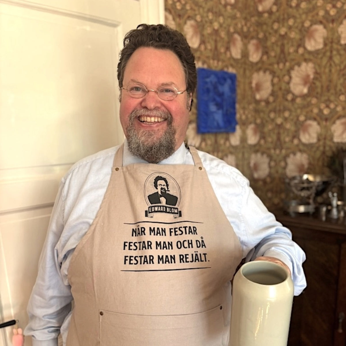 Edward Blom i sitt hem med ljusgrått förkläde med citatet "När man festar festar man och då festar man rejält."